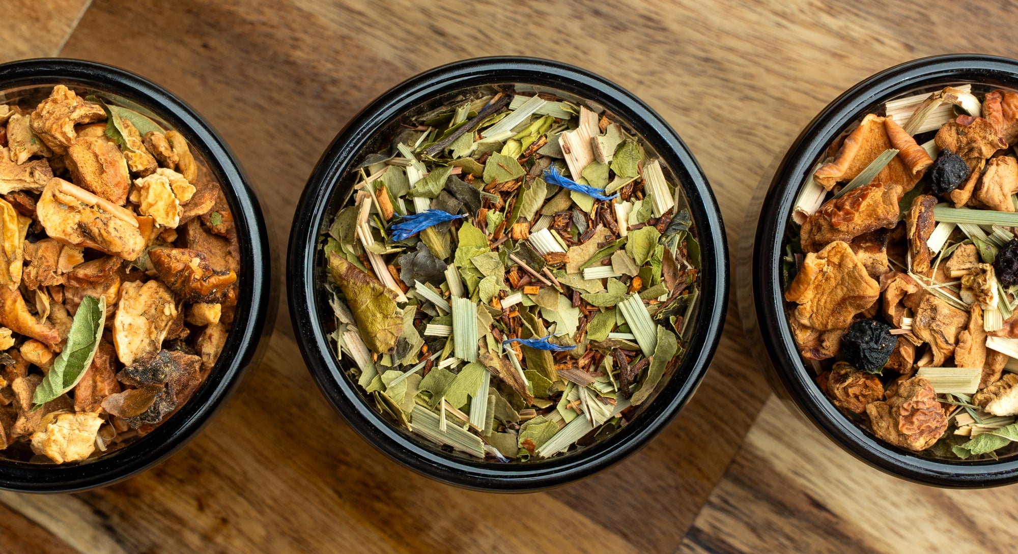 Drei lose Kräuterteemischungen mit bunten Fruchtstücken und Kräutern in drei schalen 
